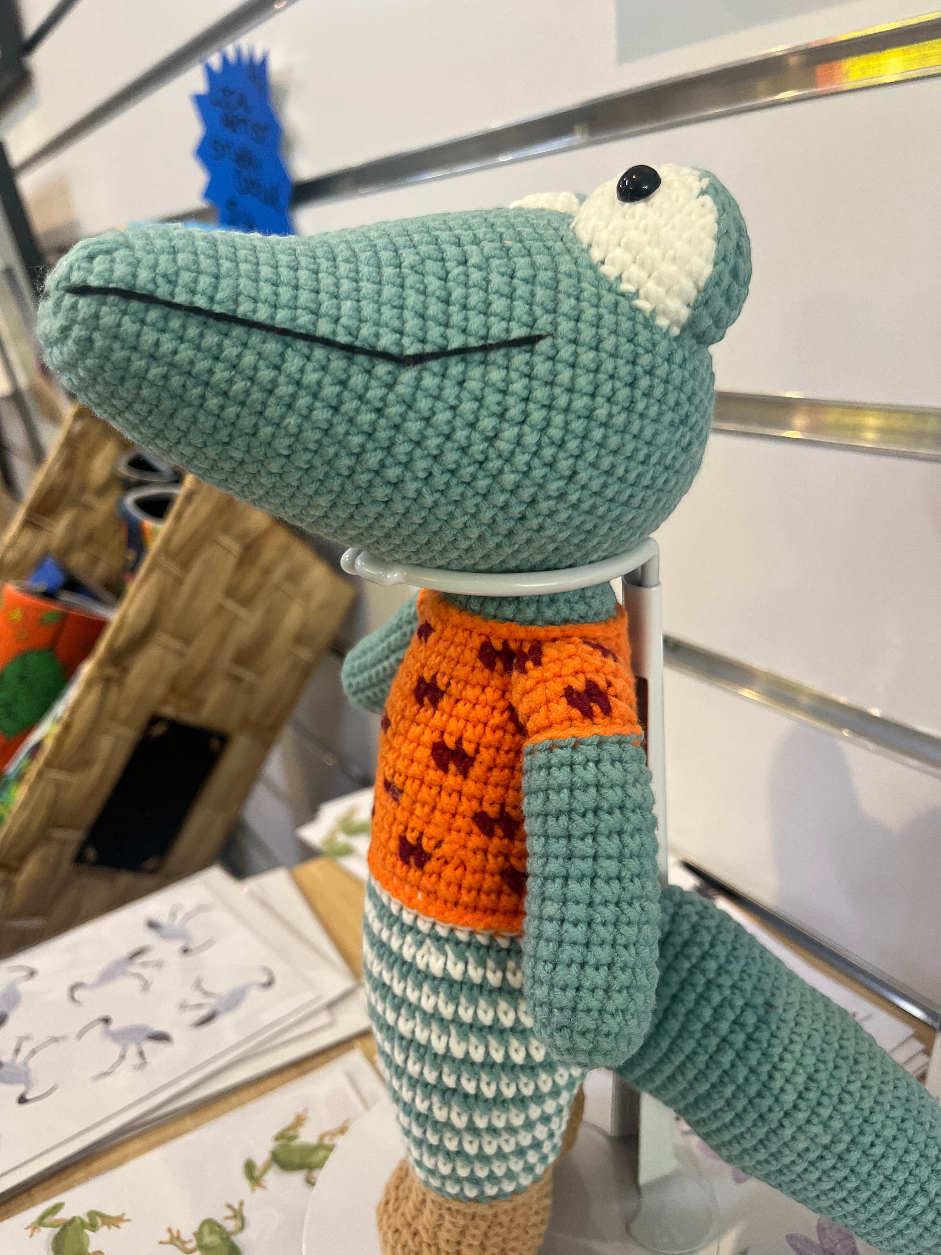 Suzie's Sunshine Dolls Calvin the Croc, a handmade crochet toy with a teal body, orange shirt, and white and teal striped pants.