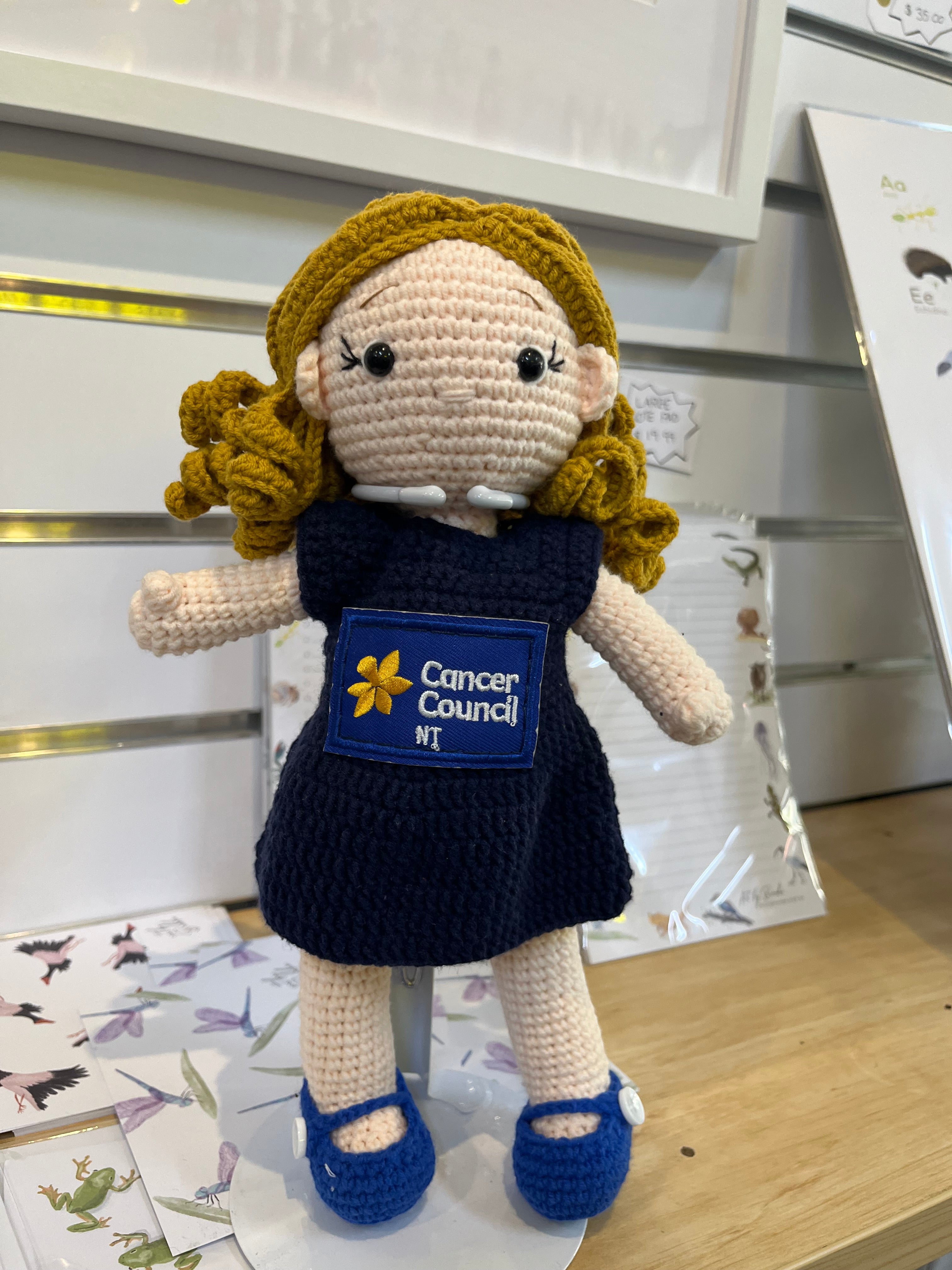 Suzie's Sunshine Dolls hand-crocheted doll in navy dress with Cancer Council NT patch, blonde hair, blue shoes.