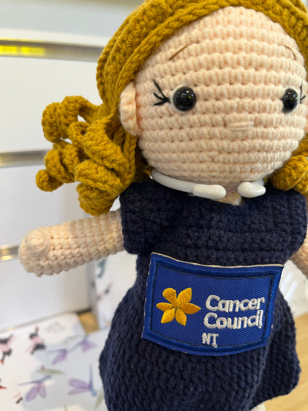 Suzie's Sunshine Dolls navy crocheted doll with blonde hair, Cancer Council NT patch, and stethoscope detail.