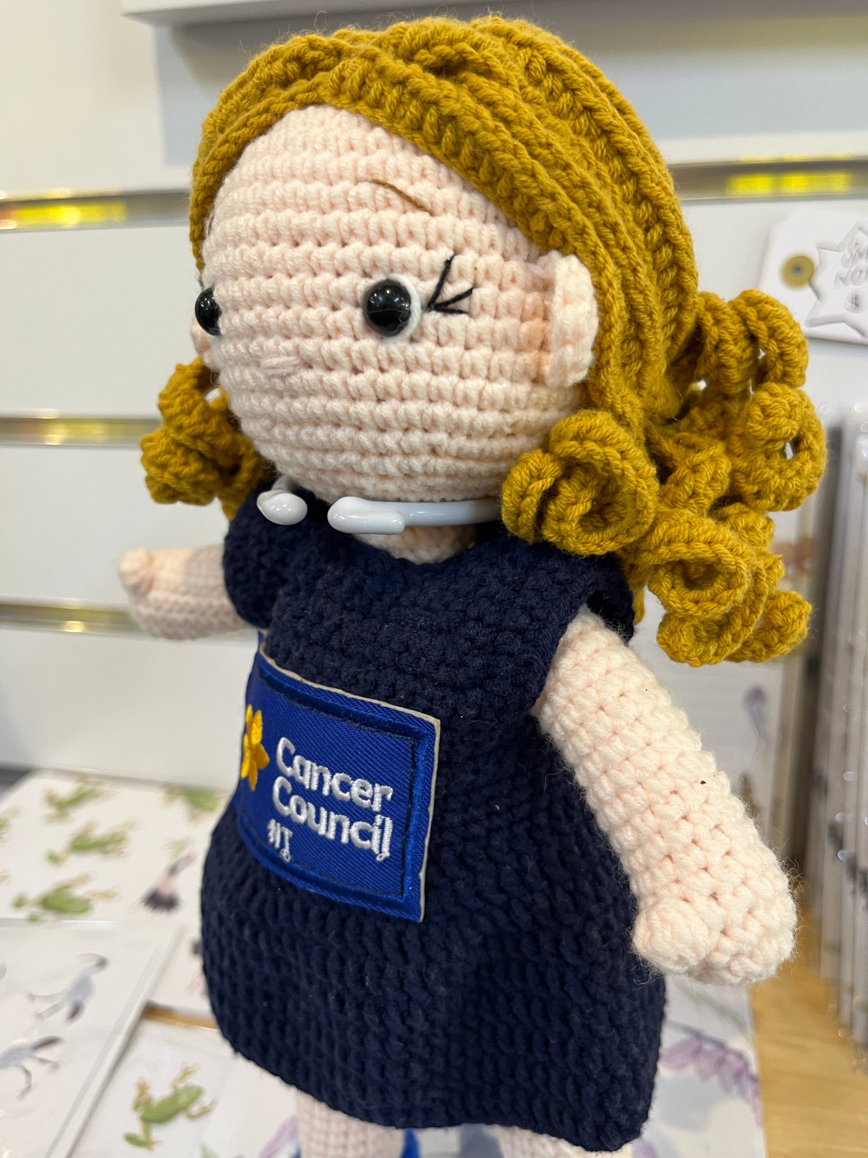 Suzie's Sunshine Dolls hand-crocheted navy doll with blonde yarn hair and Cancer Council NT patch. Educational and symbolic.