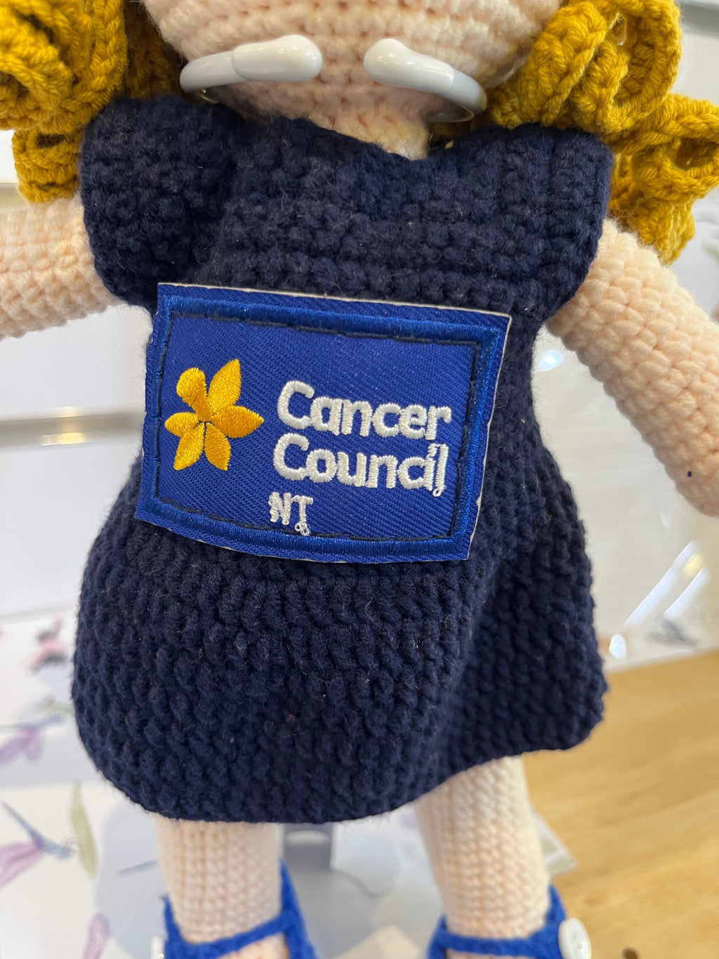 Suzie's Sunshine Dolls navy crocheted doll with Cancer Council NT patch, yellow flower detail.