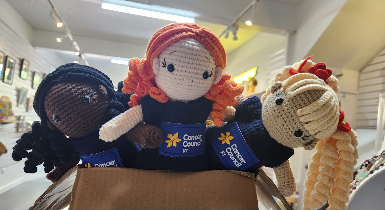 Suzie's Sunshine Dolls hand-crocheted dolls in navy dresses with Cancer Council NT patch. Diverse hair colors: black, orange, blonde.