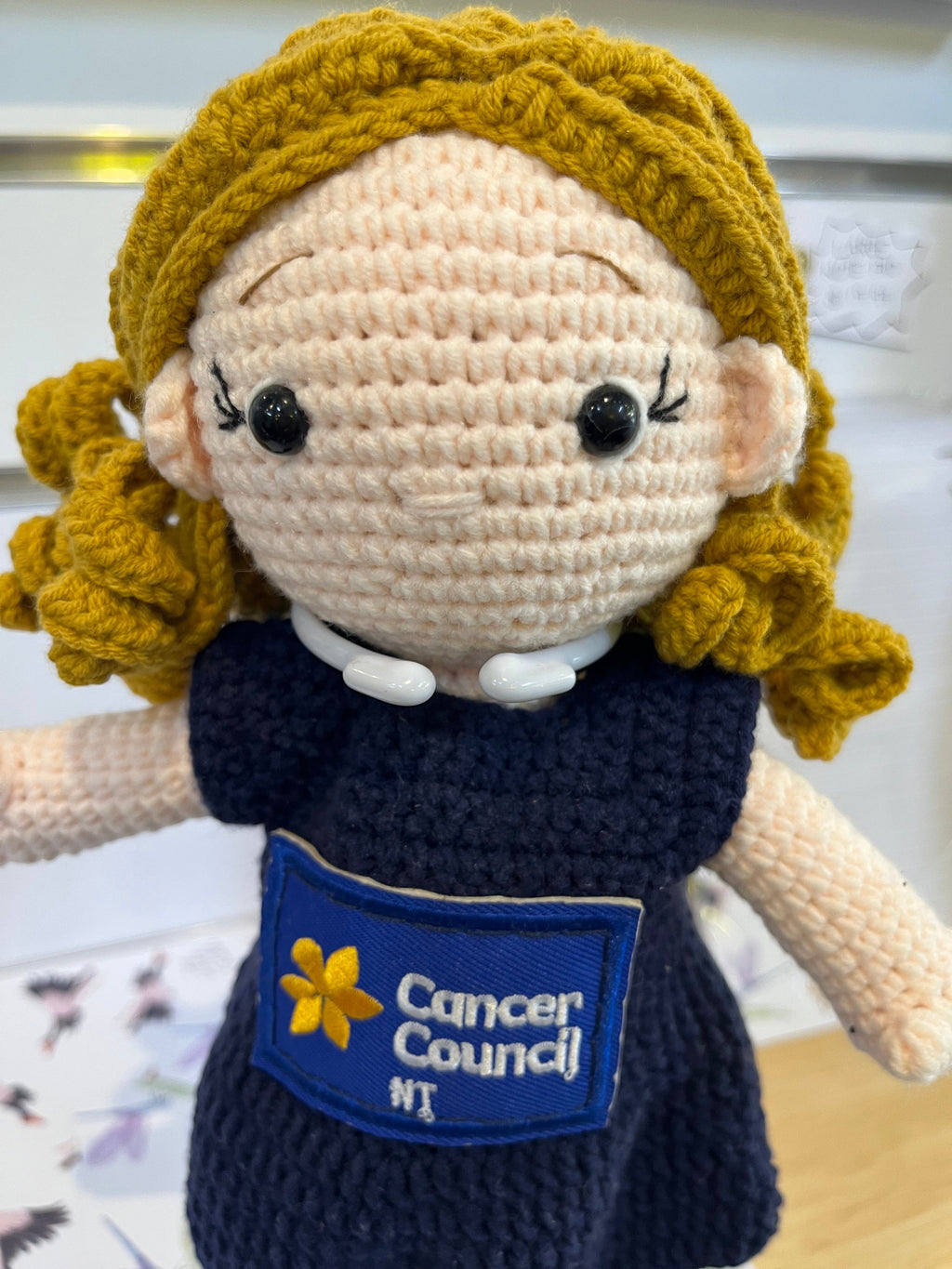 Suzie's Sunshine Dolls hand-crocheted doll in navy dress with Cancer Council NT patch. Blonde yarn hair.