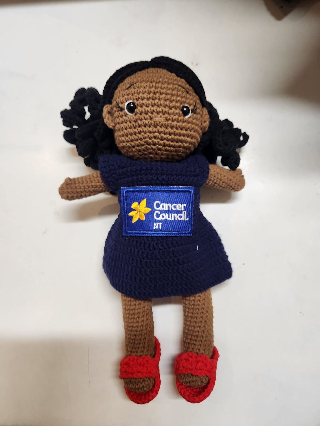Suzie's Sunshine Dolls navy crocheted doll with Cancer Council NT patch and red shoes. Hand-made yarn toy.