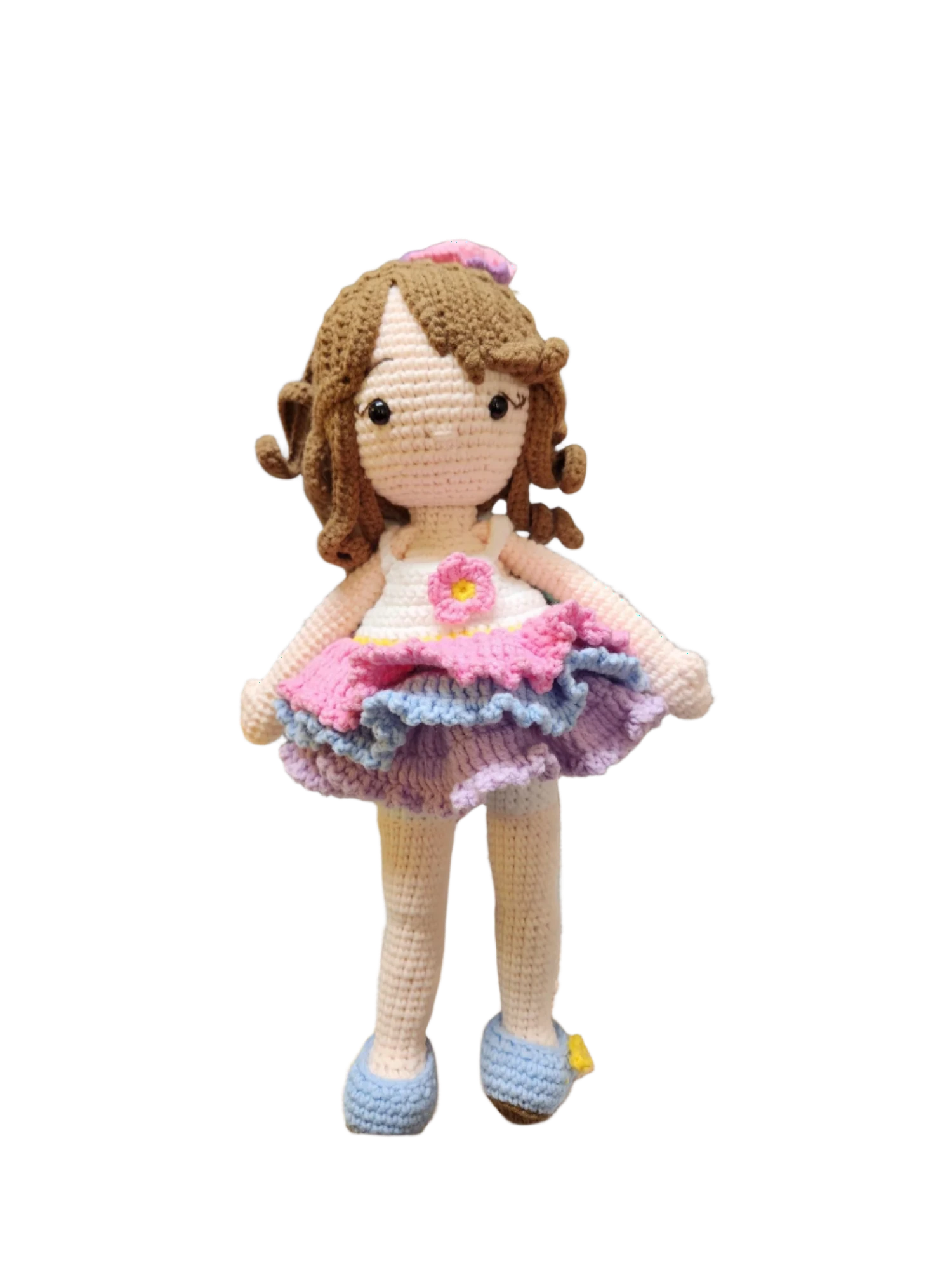 Suzie's Sunshine Dolls Cleo, a handmade crochet doll with brown yarn curls, wearing a pink, purple, and blue ruffled dress and blue shoes.