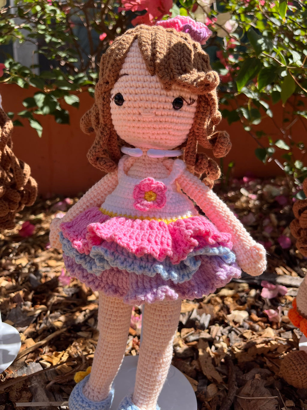 Suzie's Sunshine Dolls Cleo, a handmade crochet ballerina doll with brown curls, a pink, purple, and blue ruffled dress, and a flower applique.