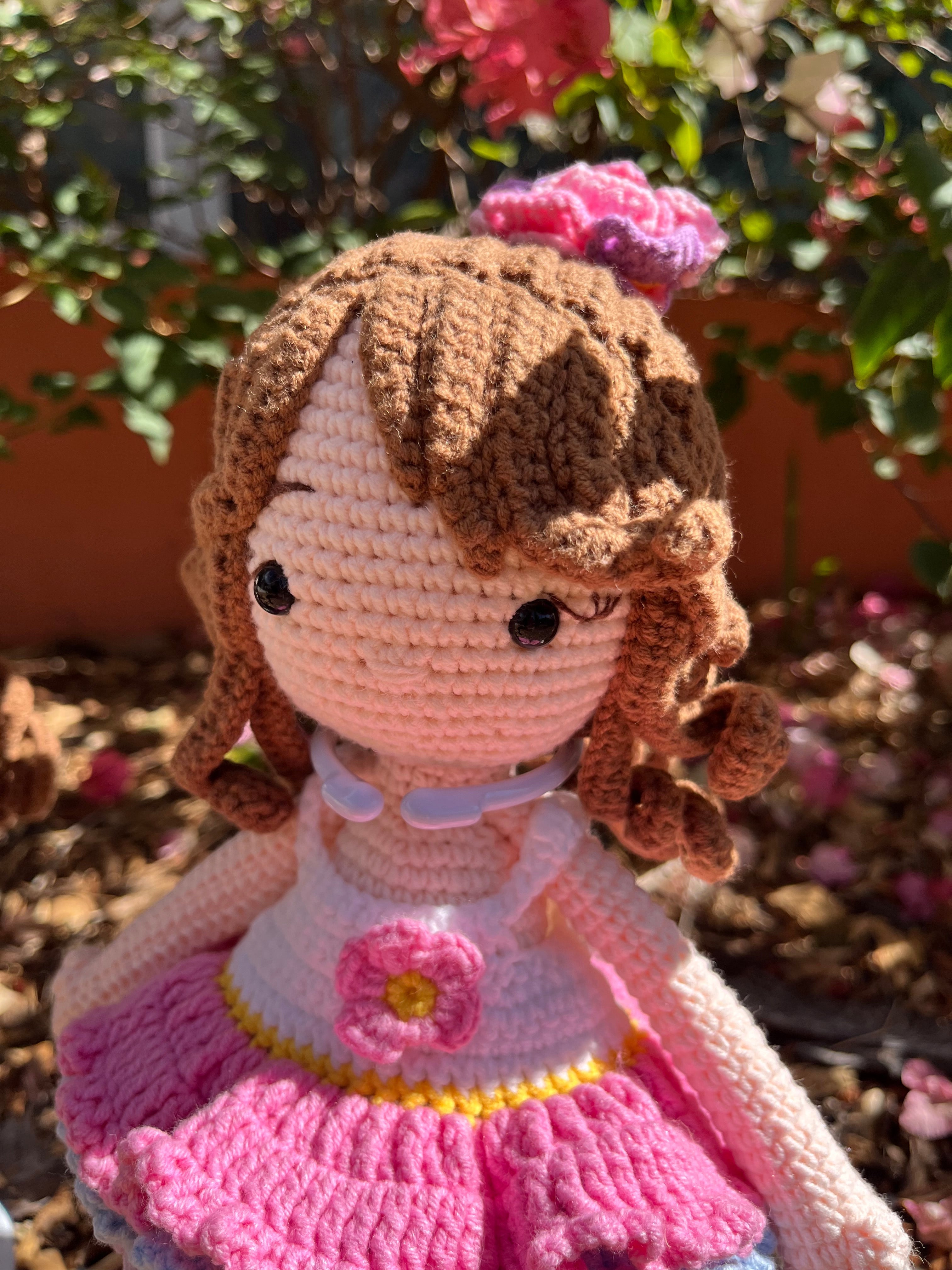Suzie's Sunshine Dolls Cleo, a handmade crochet doll with brown yarn curls, wearing a pink, purple, and blue ruffled dress with a flower applique.