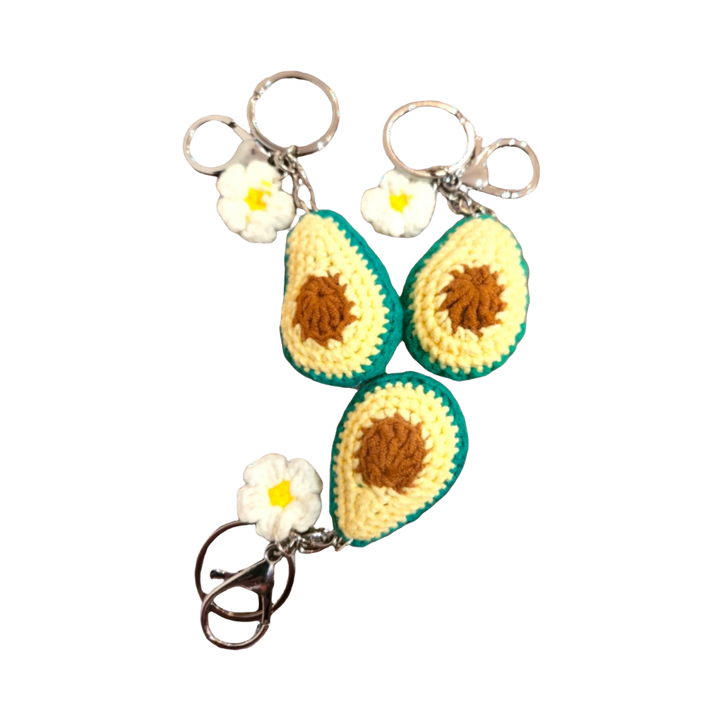 Suzie's Sunshine Dolls handmade crochet avocado keychains with white flowers and metal clasps. Yellow, brown, and green yarn.