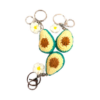Suzie's Sunshine Dolls handmade crochet avocado keychains with white flowers and metal clasps. Yellow, brown, and green yarn.