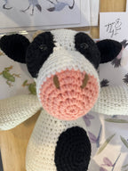 Suzie's Sunshine Dolls Daisy the Cow, a handmade crochet toy with black and white patches, pink snout, and black button eyes.