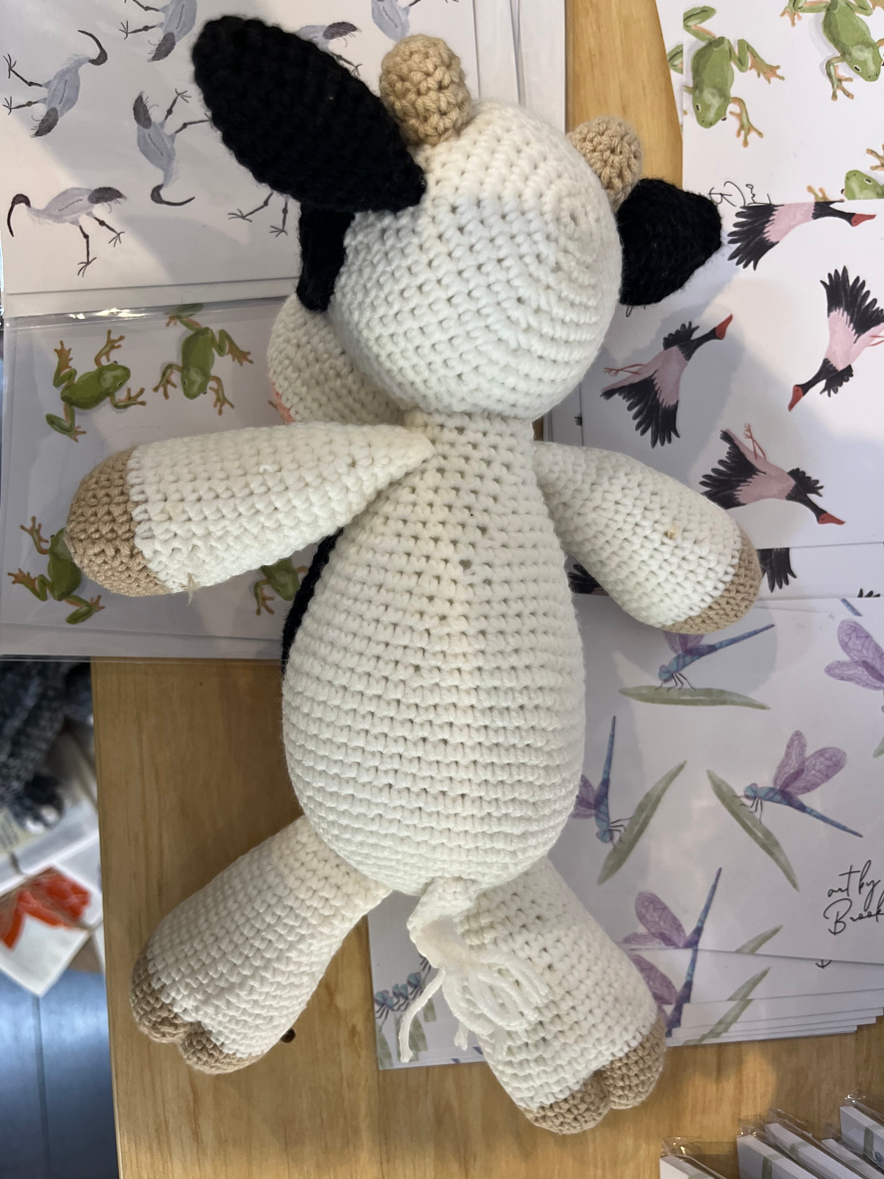 Suzie's Sunshine Dolls Daisy the Cow, a handmade crochet toy with black and white spots, beige ears and hooves, and a pink snout.
