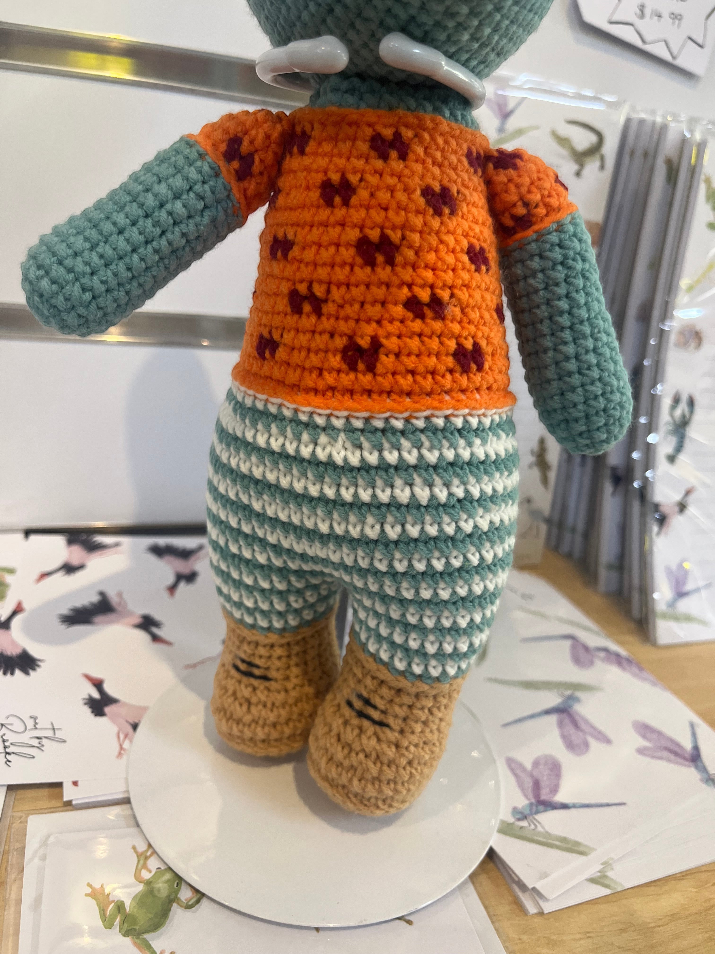 Suzie's Sunshine Dolls Calvin the Croc handmade crochet toy, orange shirt, blue striped shorts, tan feet.