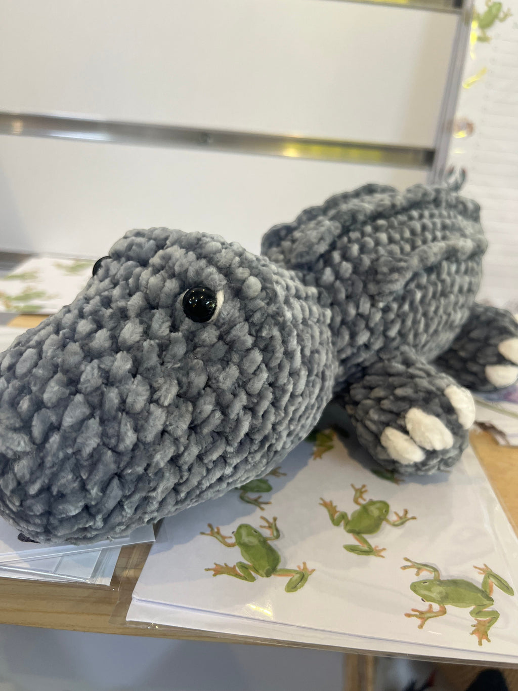 Suzie's Sunshine Dolls Kurtis the Croc, a handmade grey crochet crocodile plush toy with white toes and stitched smile.