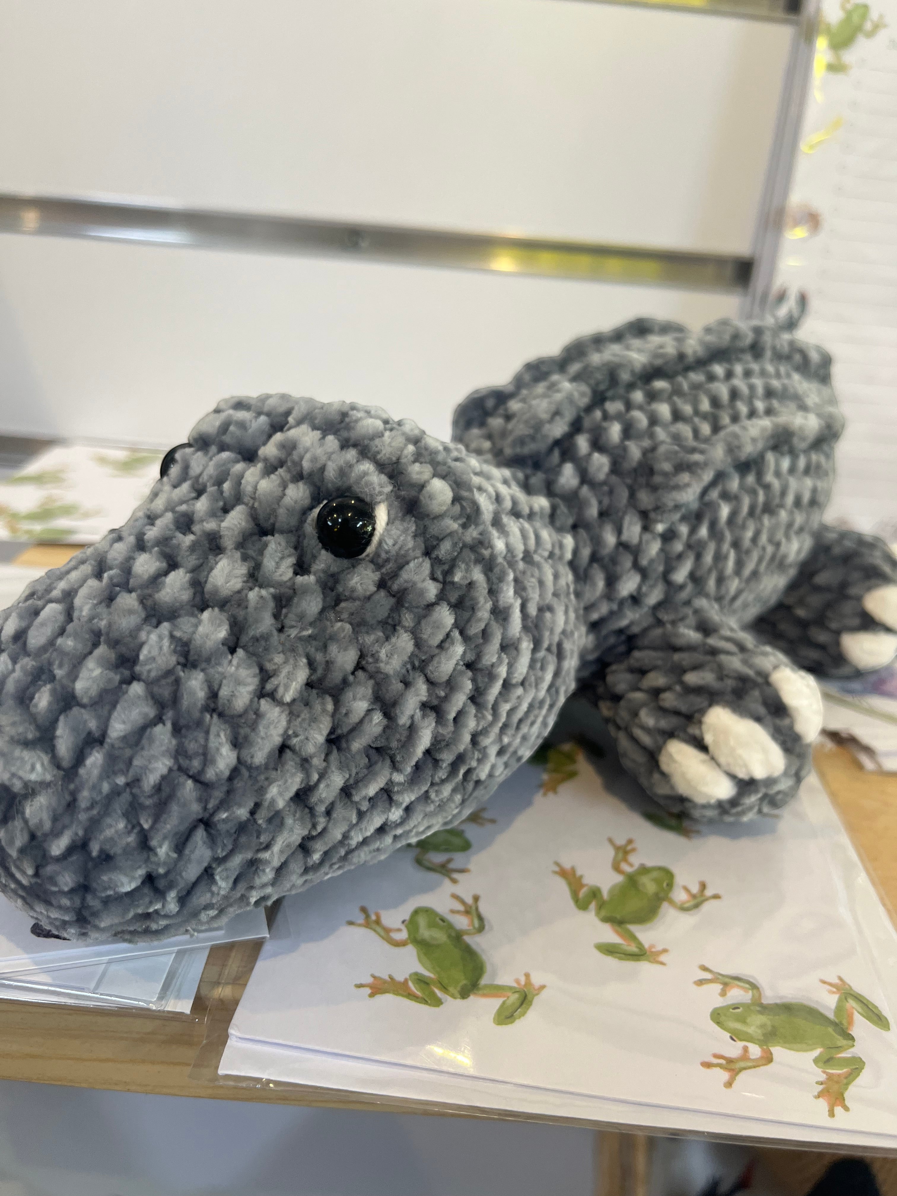 Suzie's Sunshine Dolls Kurtis the Croc, a handmade grey crochet crocodile plush toy with white toes and stitched smile.