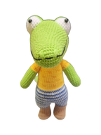 Suzie's Sunshine Dolls Calvin the Croc, a handmade crochet toy with a green body, orange shirt, and blue striped shorts.