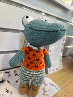 Suzie's Sunshine Dolls Calvin the Croc, a handmade crochet toy with a teal body, orange shirt, and striped pants.