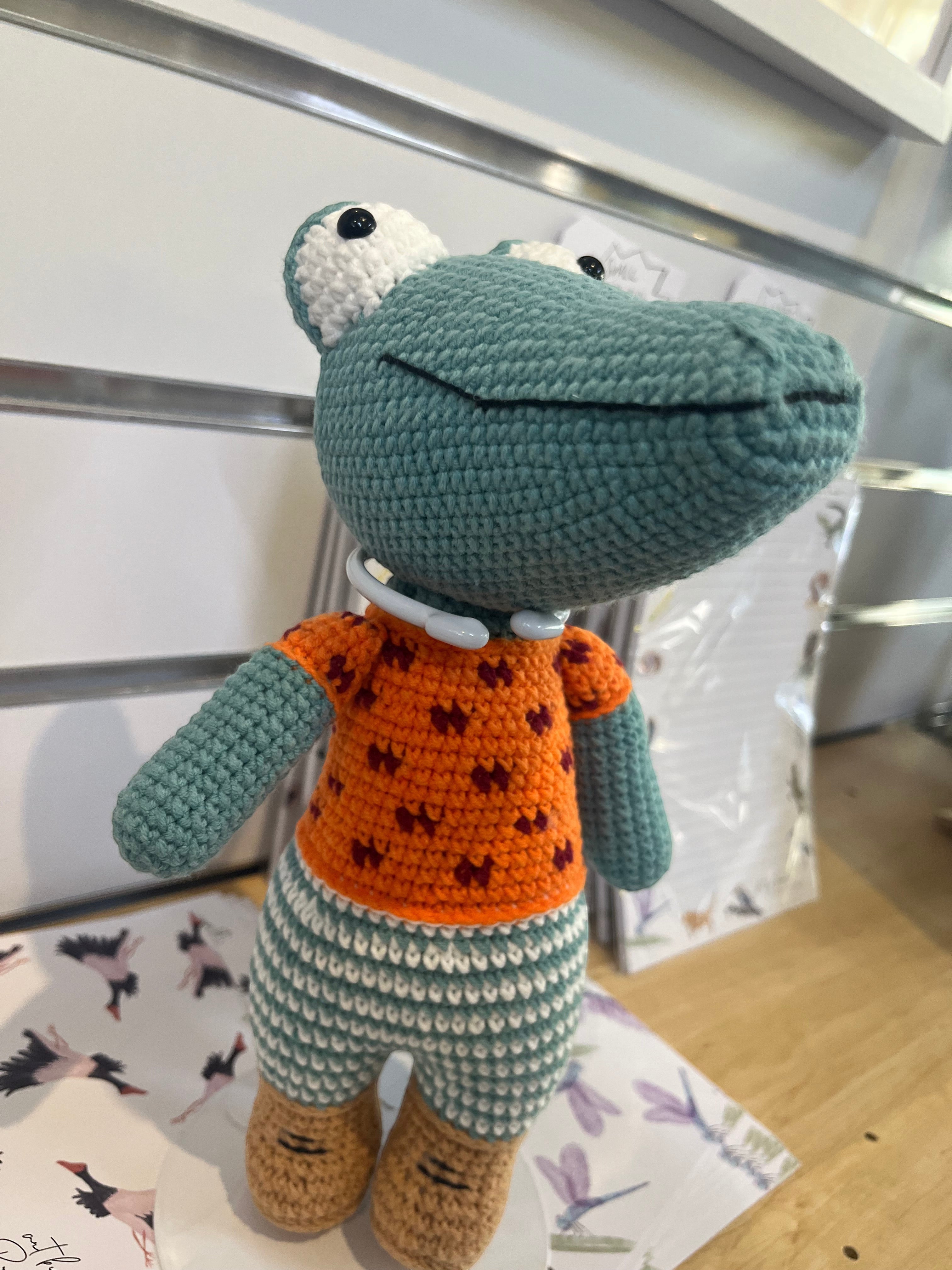 Suzie's Sunshine Dolls Calvin the Croc, a handmade crochet toy with a teal body, orange shirt, and striped pants.