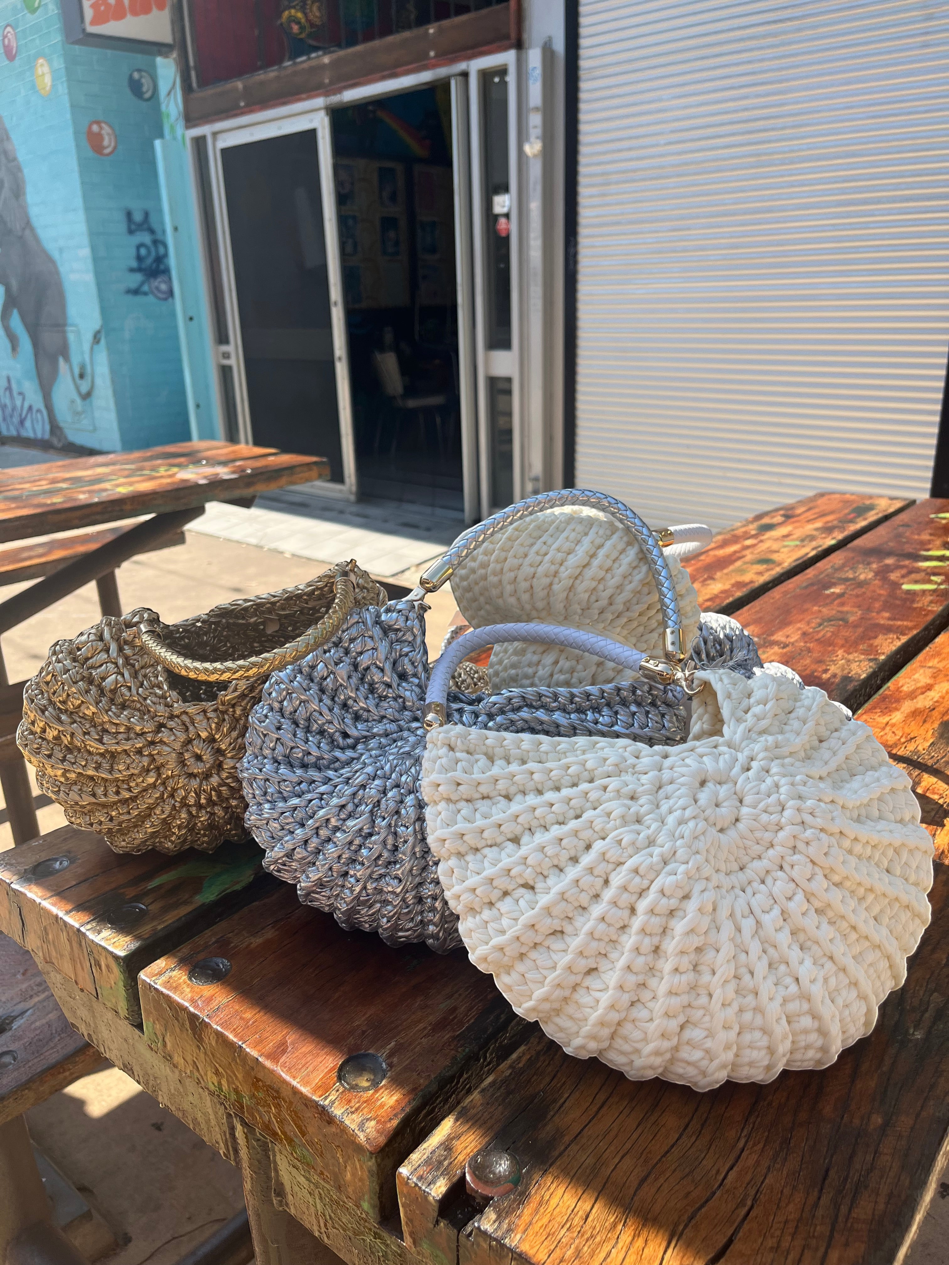 Suzie's Sunshine Dolls textured crochet shoulder bag in silver, white, and gold with braided handles.