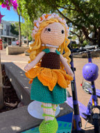 Suzie's Sunshine Dolls Daisy crochet doll with blonde yarn hair, sunflower skirt, green shoes, and floral crown.