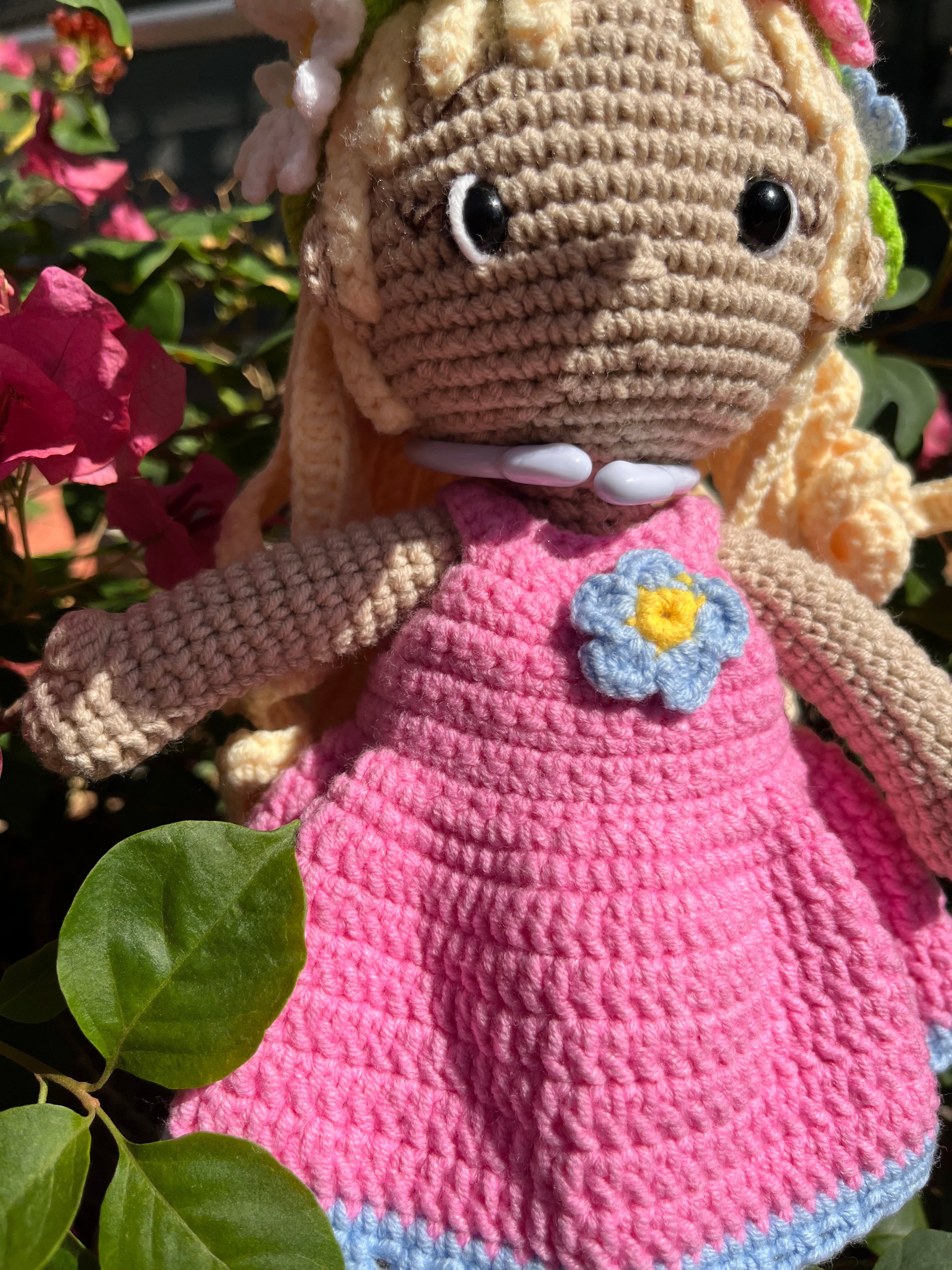 Suzie's Sunshine Dolls Delilah, a handmade crochet doll with blonde hair, wearing a pink dress with blue trim and a flower crown.