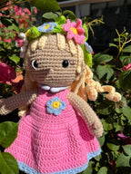 Suzie's Sunshine Dolls Delilah, a handmade crochet doll with blonde curls, wearing a pink dress with blue trim and a flower crown.