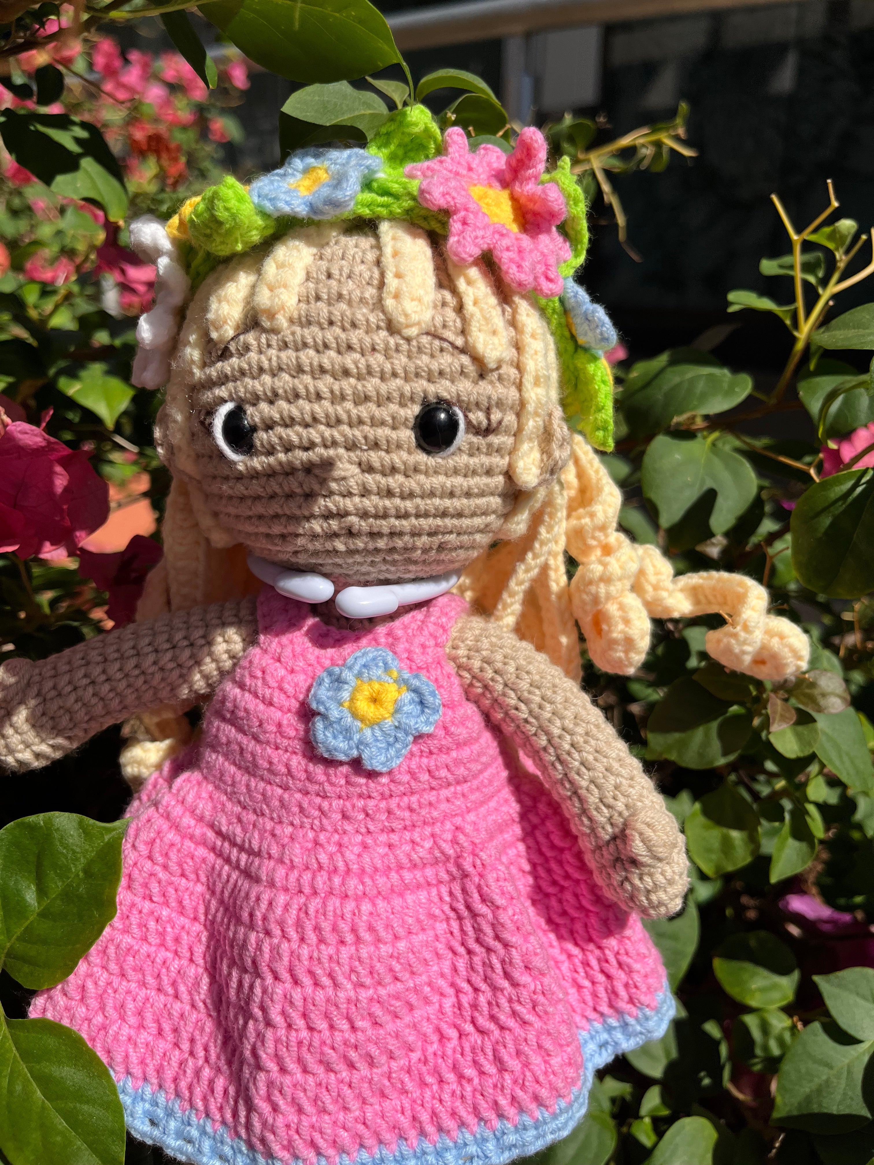 Suzie's Sunshine Dolls Delilah, a handmade crochet doll with blonde curls, wearing a pink dress with blue trim and a flower crown.