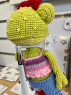 Suzie's Sunshine Dolls Frieda the Frog crochet doll with googly eyes, red bow, pastel crop top, denim shorts, and red sneakers.
