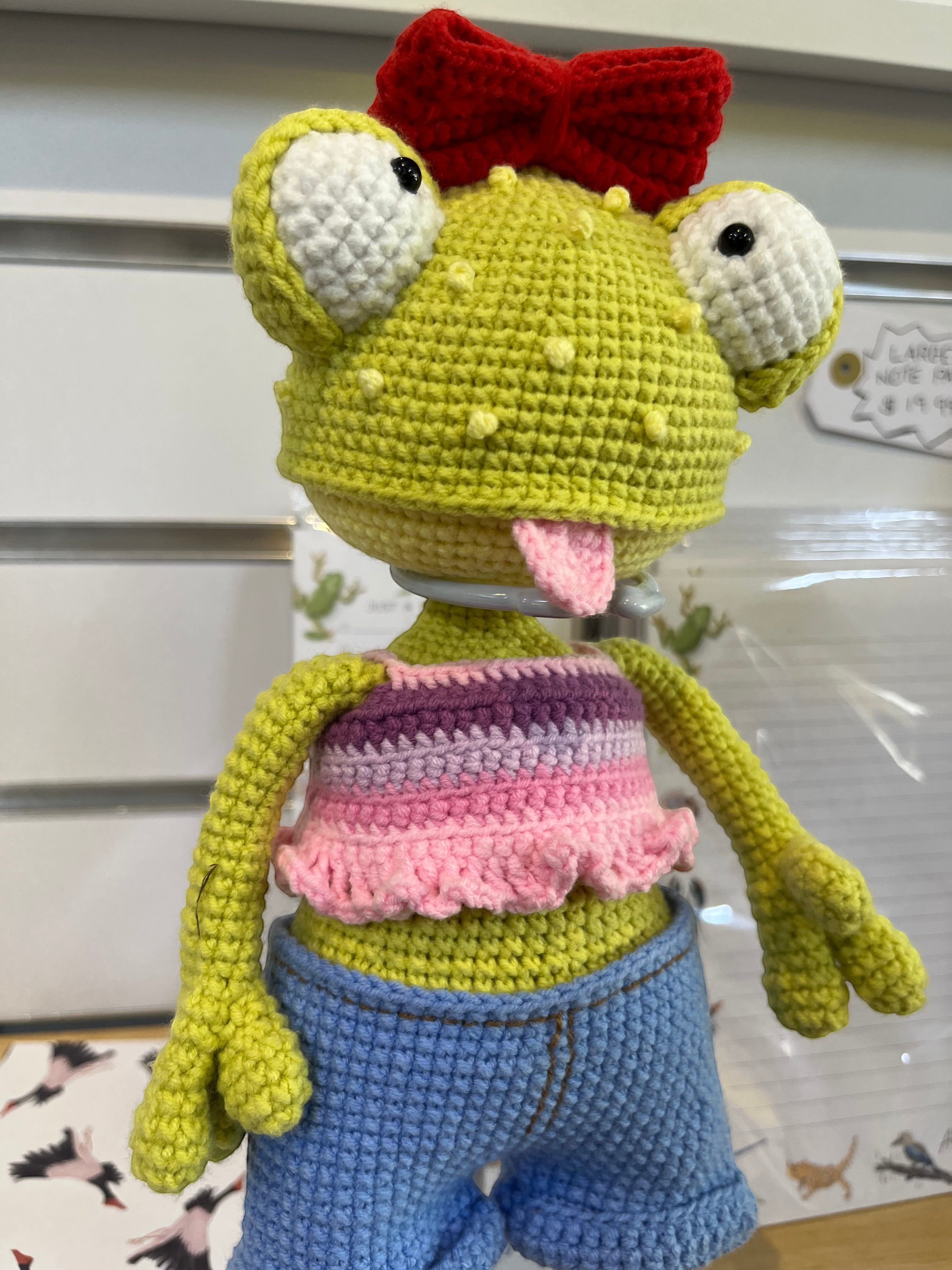 Suzie's Sunshine Dolls Frieda the Frog crochet doll with big googly eyes, red bow, and tongue out. Wears striped crop top and denim shorts.