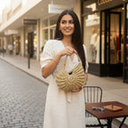 Suzie's Sunshine Dolls gold woven shell handbag with braided handle, worn by a woman in a cream dress.