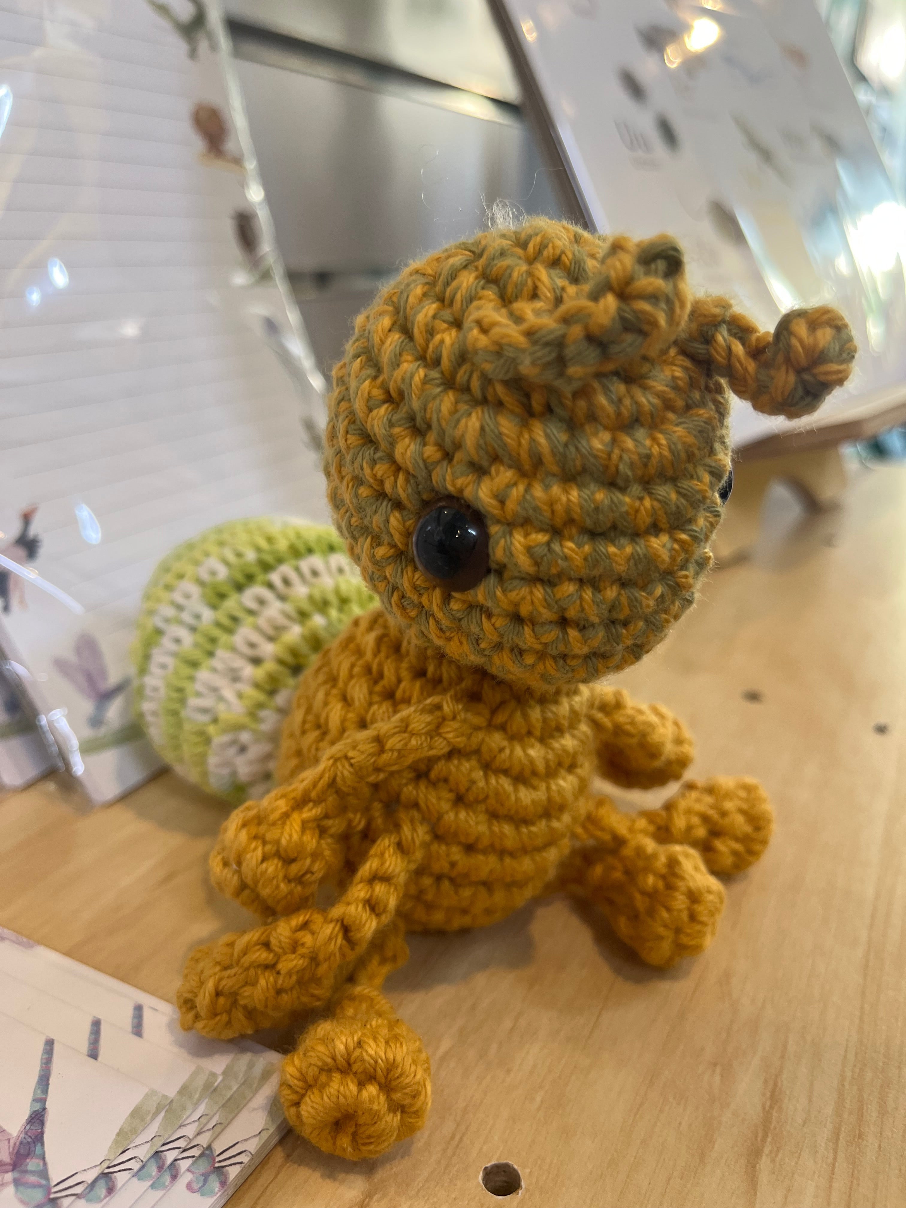 Suzie's Sunshine Dolls Gertrude the Green Ant crochet toy, yellow-green yarn body, black eyes, antennae, and striped tail.