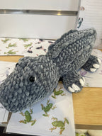 Suzie's Sunshine Dolls Kurtis the Croc, a grey plush crocodile toy with white toes and stitched smile.