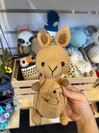 Suzie's Sunshine Dolls Kirsty the Kangaroo, a handmade crochet toy in tan yarn with a joey in her pouch. Features tall ears and black eyes.