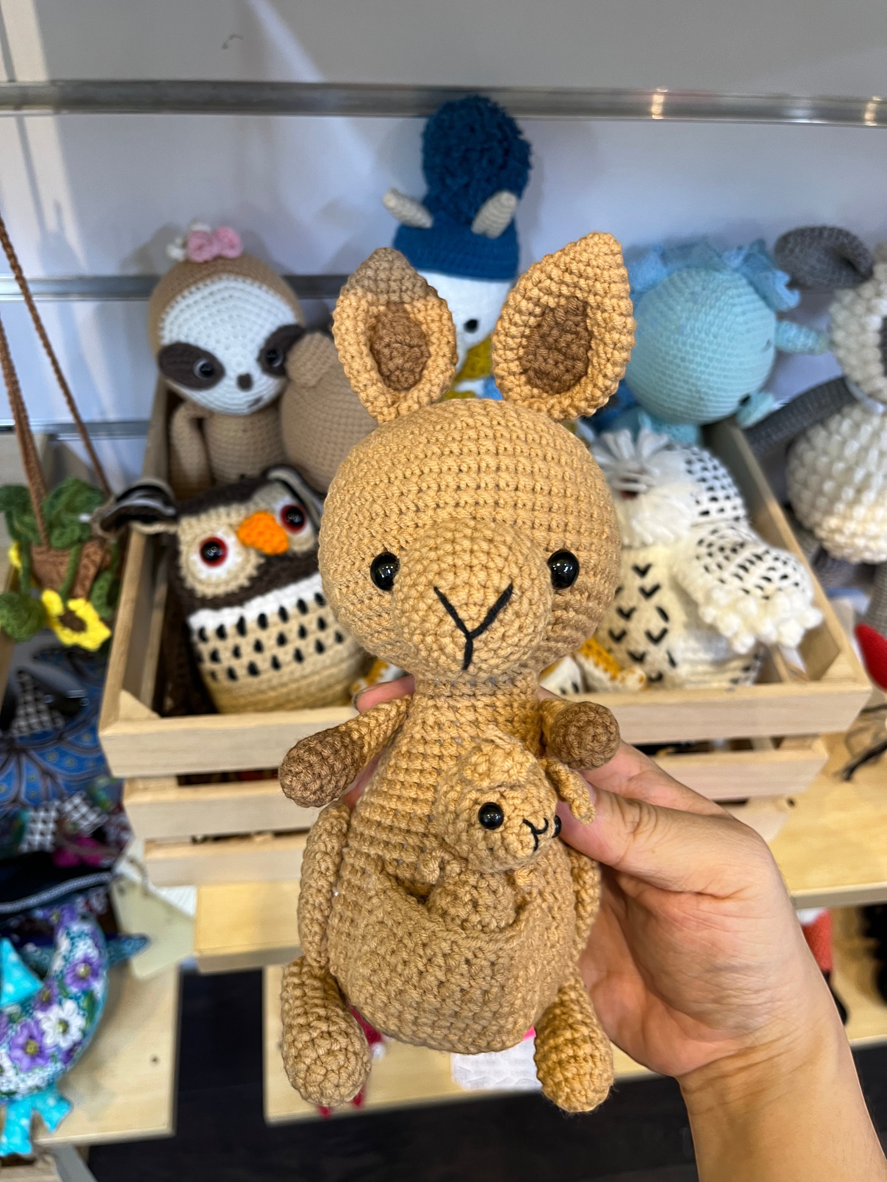 Suzie's Sunshine Dolls Kirsty the Kangaroo, a handmade crochet toy in tan yarn with a joey in her pouch. Features tall ears and black eyes.