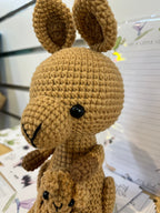 Suzie's Sunshine Dolls Kirsty the Kangaroo, a handmade crochet toy in tan yarn with a joey in her pouch. Features black button eyes and tall ears.