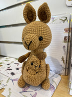 Suzie's Sunshine Dolls Kirsty the Kangaroo, a handmade crochet toy in tan yarn with a joey in her pouch. Features large ears and black button eyes.