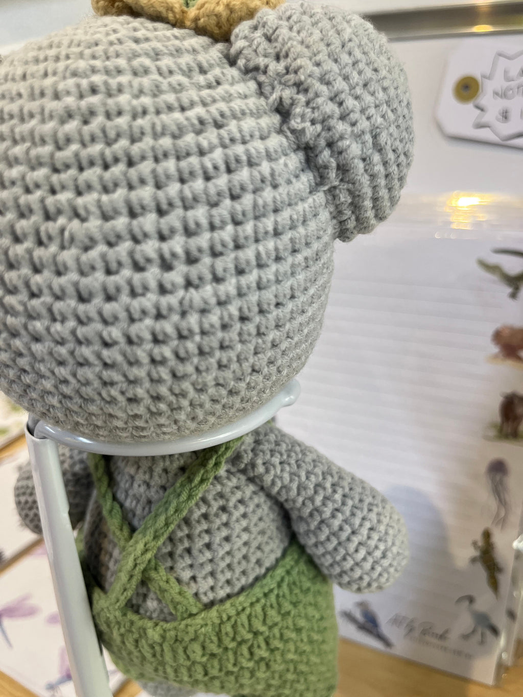 Suzie's Sunshine Dolls Kolby the Koala, a grey crochet stuffed animal wearing green overalls and a straw hat.