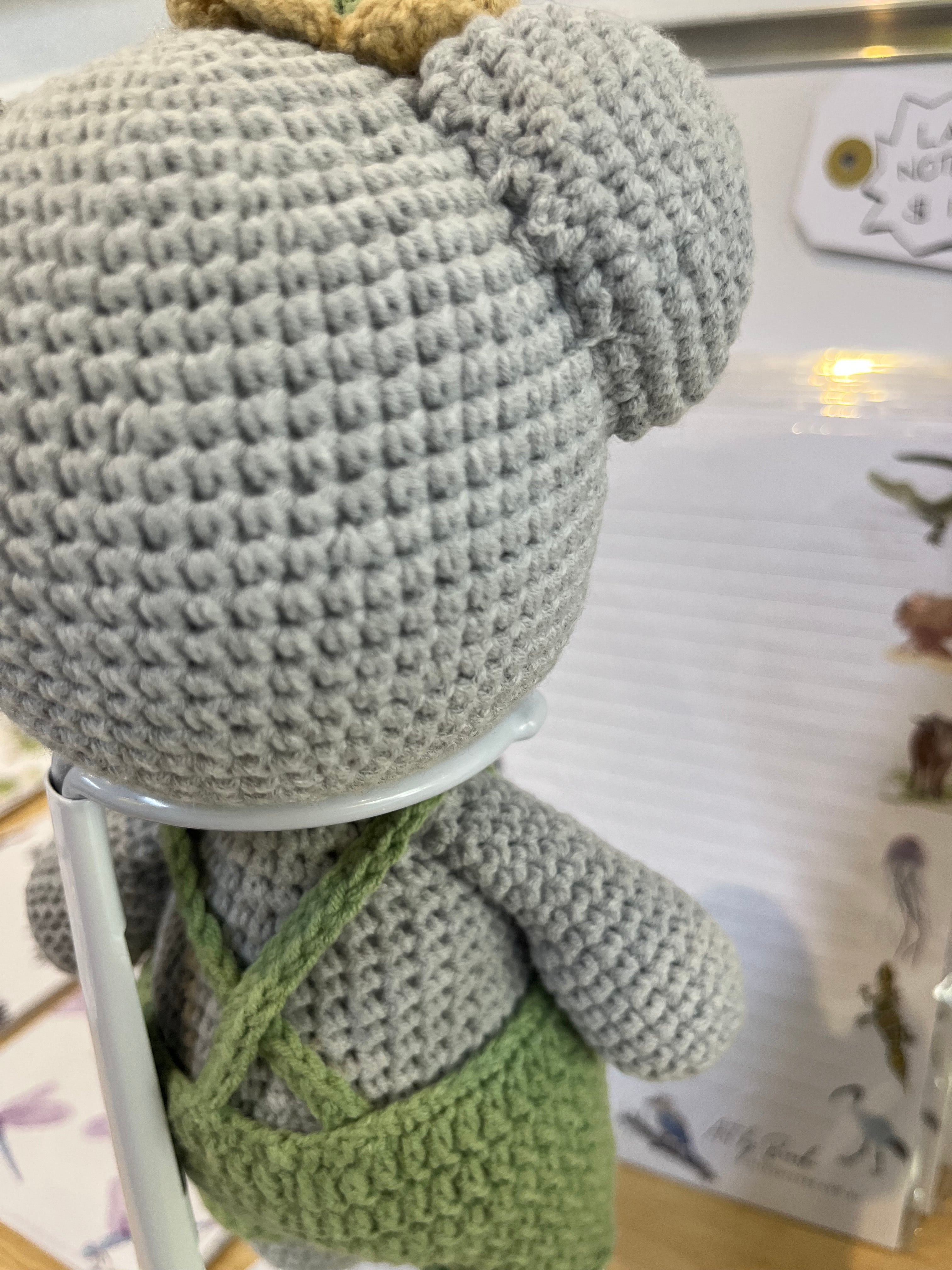 Suzie's Sunshine Dolls Kolby the Koala, a grey crochet stuffed animal wearing green overalls and a straw hat.