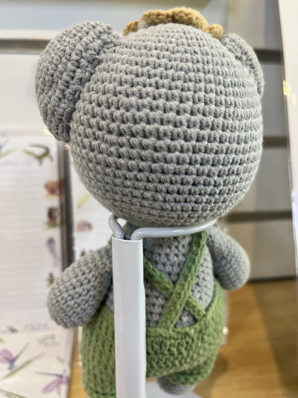 Suzie's Sunshine Dolls Kolby the Koala, a grey crocheted stuffed animal wearing green overalls and a straw hat.