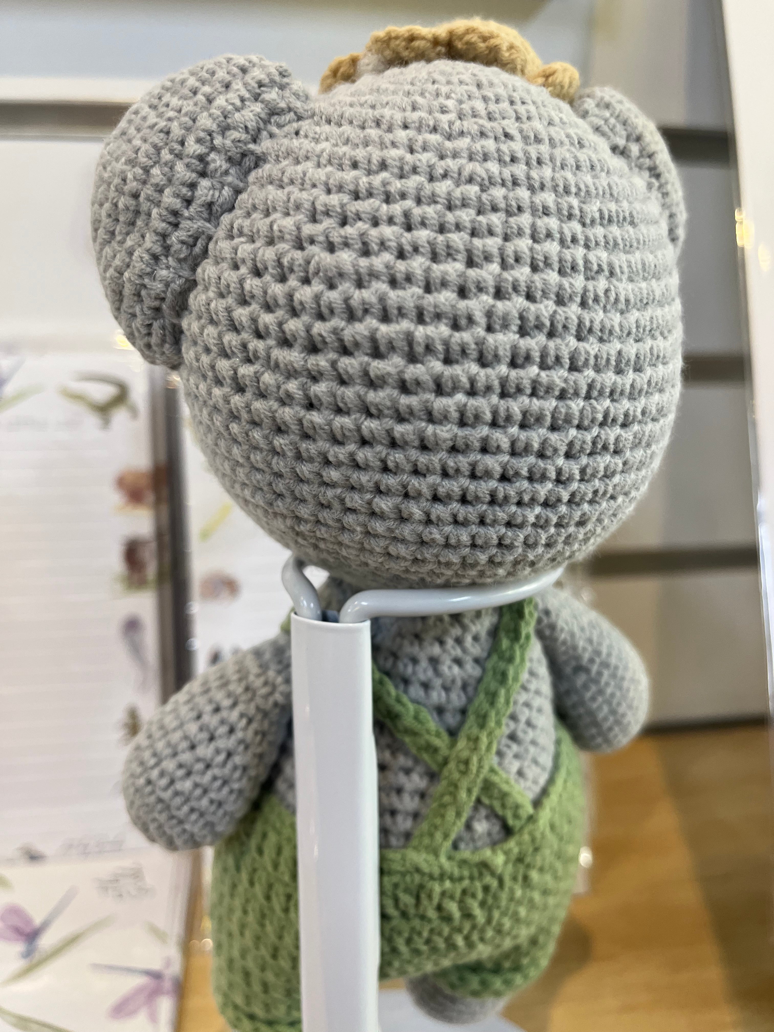 Suzie's Sunshine Dolls Kolby the Koala, a grey crocheted stuffed animal wearing green overalls and a straw hat.
