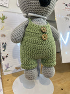 Suzie's Sunshine Dolls Kolby the Koala, a grey crocheted stuffed animal wearing green overalls with wooden buttons and a straw hat.