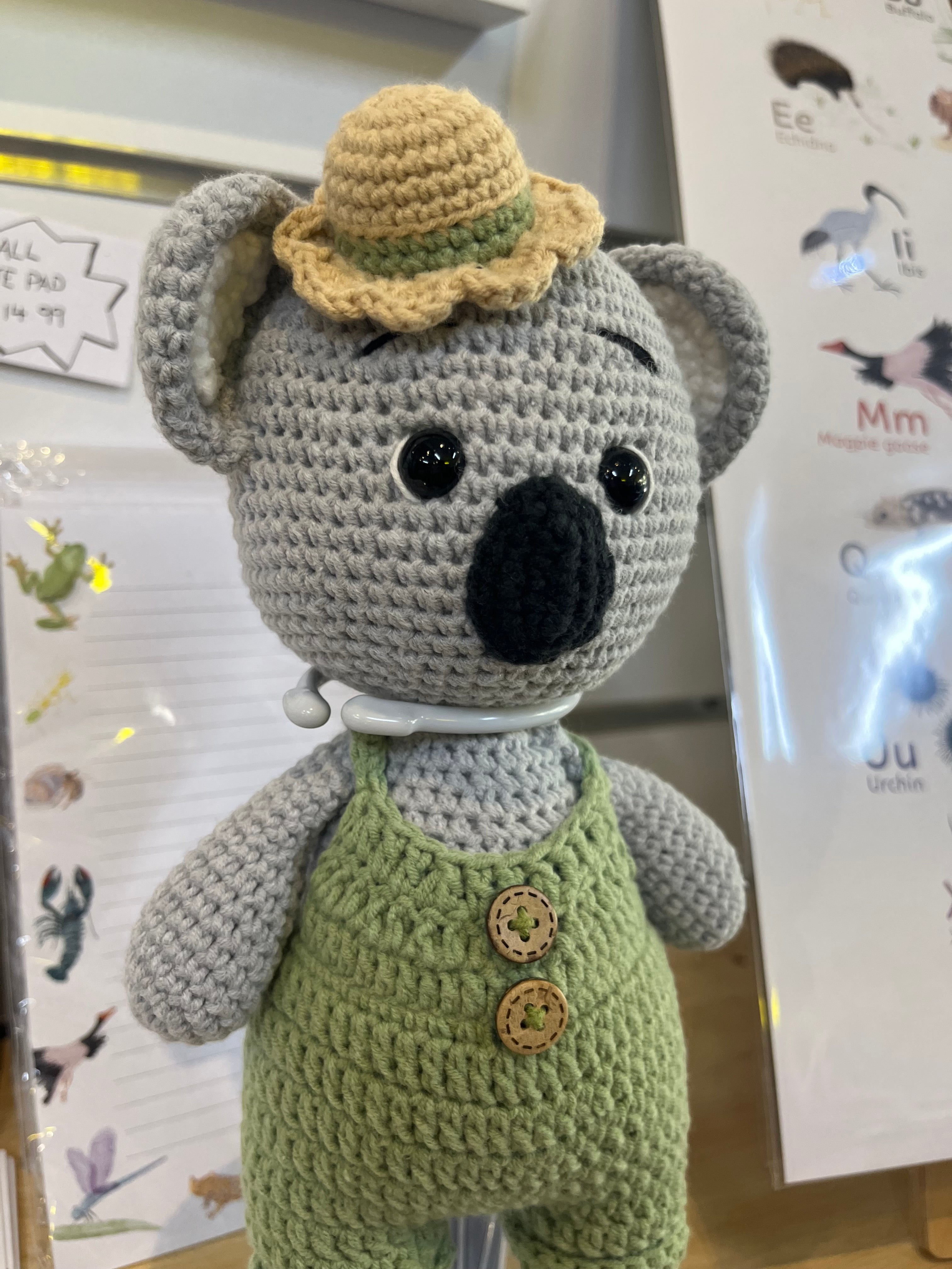 Suzie's Sunshine Dolls Kolby the Koala, a grey crocheted doll wearing green overalls and a straw hat.