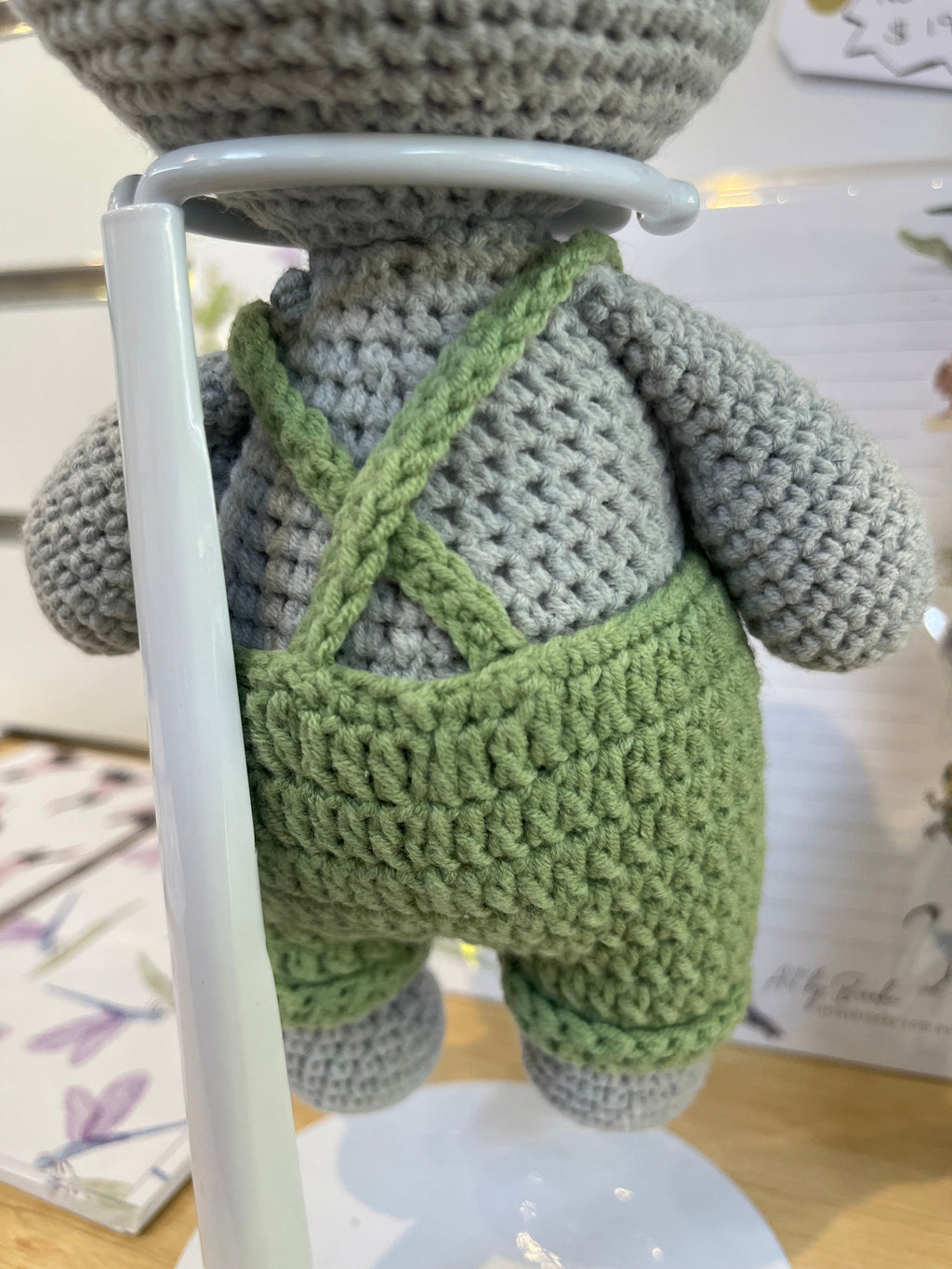 Suzie's Sunshine Dolls Kolby the Koala, a grey crocheted stuffed animal wearing green overalls and a straw hat.