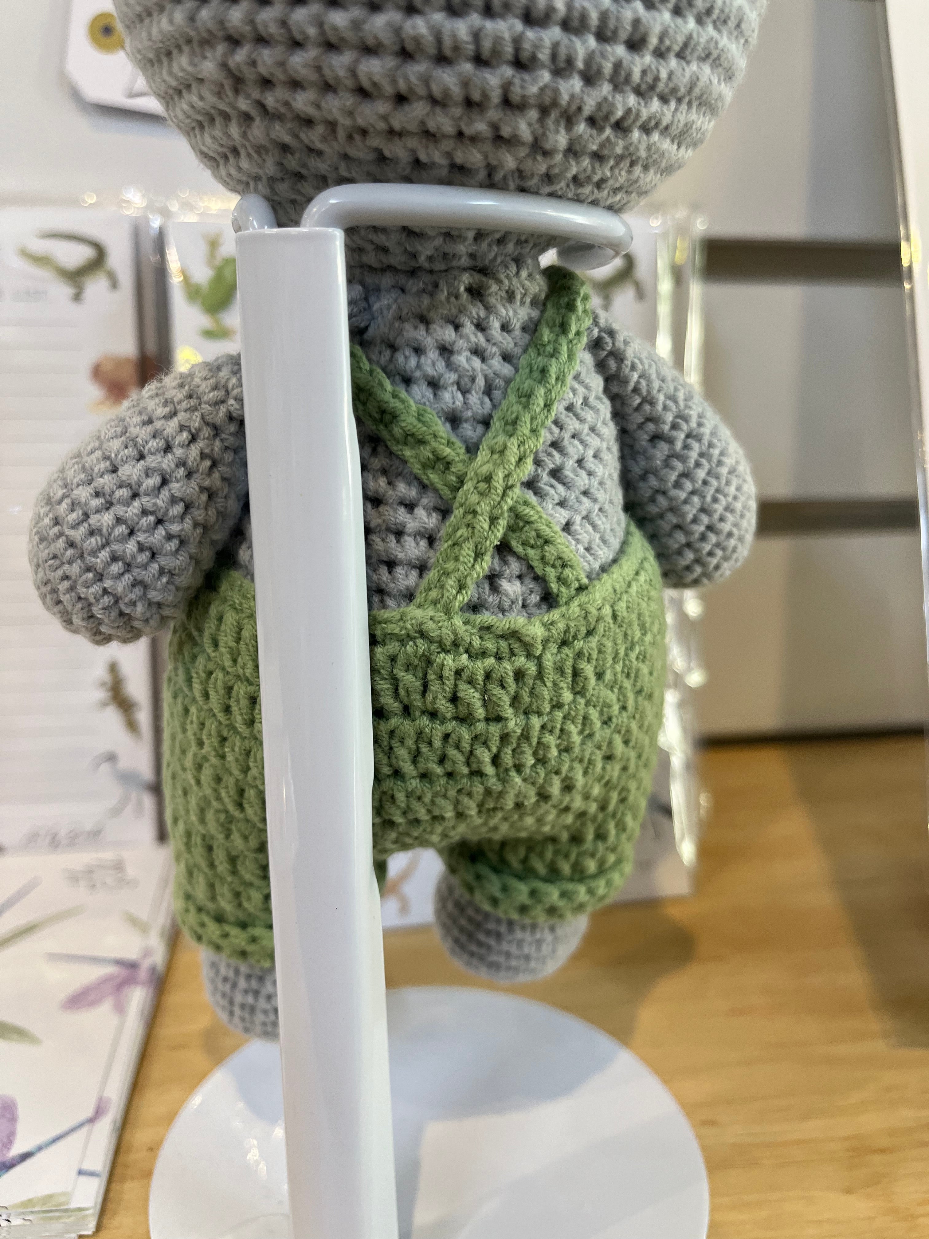 Suzie's Sunshine Dolls Kolby the Koala, a grey crocheted stuffed animal wearing green overalls and a straw hat.