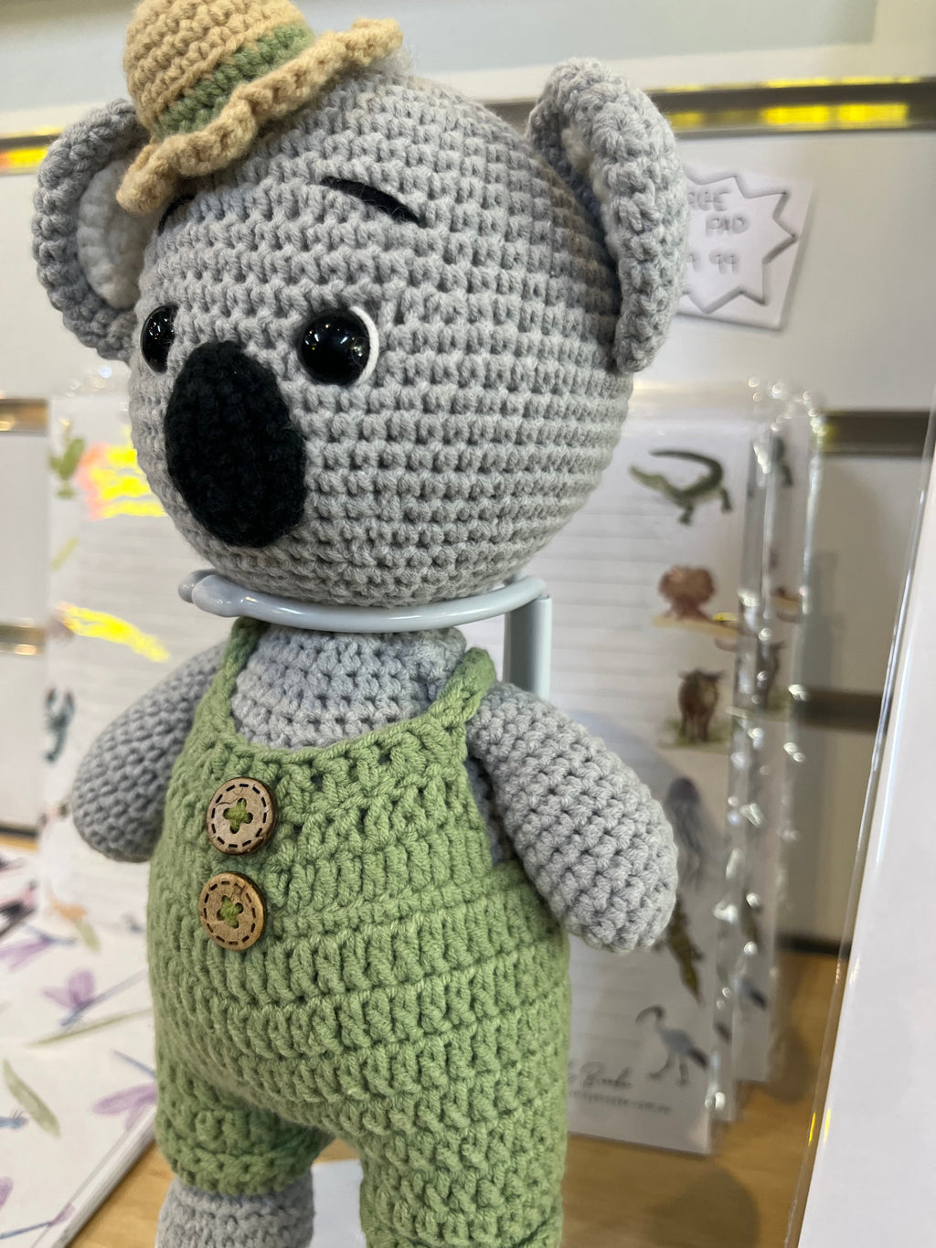 Suzie's Sunshine Dolls Kolby the Koala, a grey crocheted stuffed toy wearing green overalls and a straw hat.