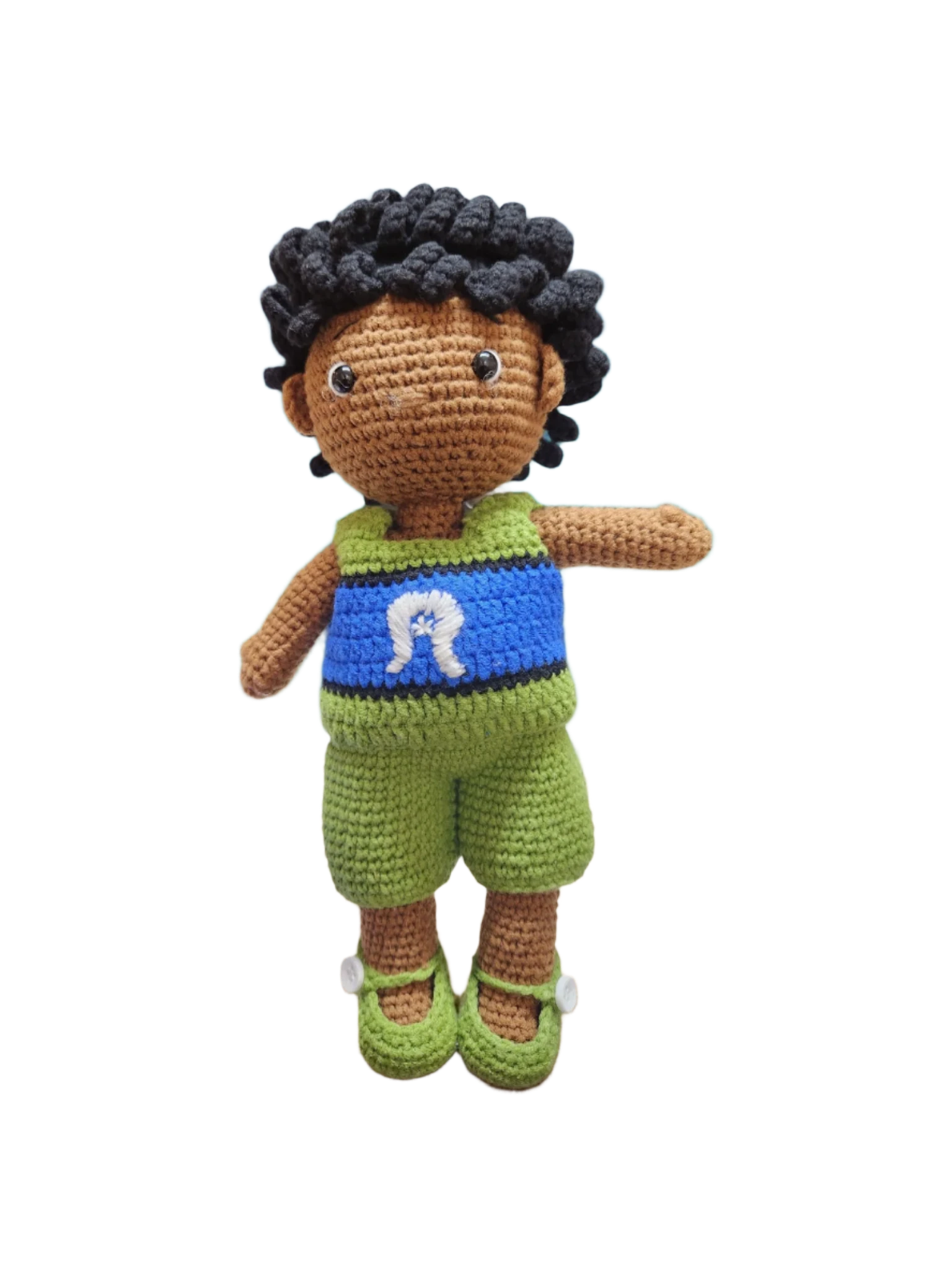 Suzie's Sunshine Dolls Malakai, a crocheted doll with short black hair, wearing green shorts and a blue top with a white Dhari headdress detail.