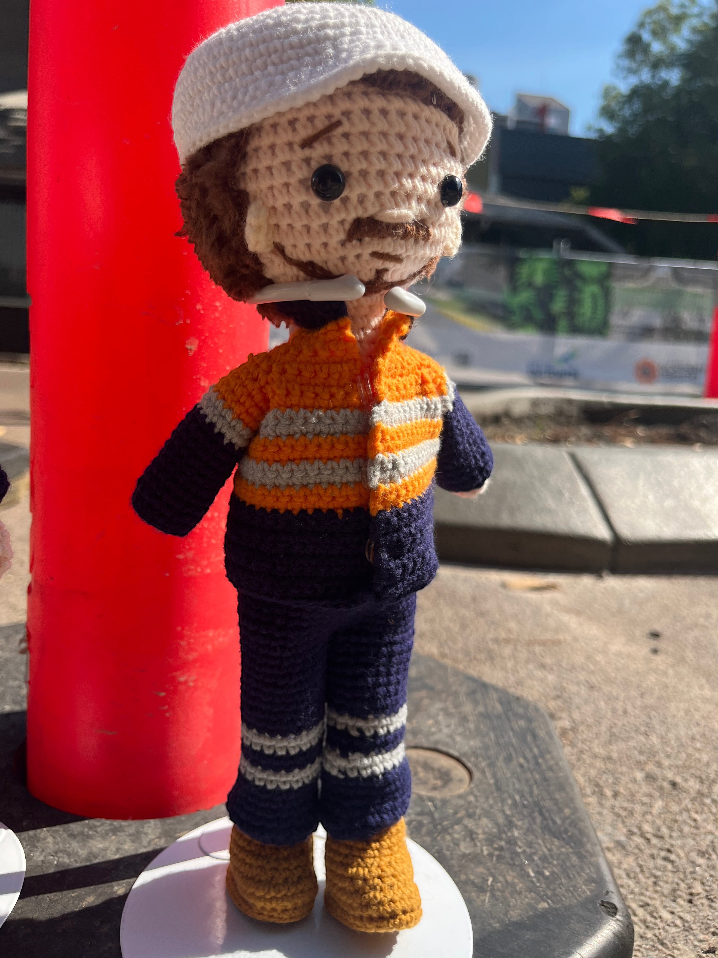 Suzie's Sunshine Dolls Miner/Tradie doll in orange hi-vis uniform, navy pants, and white hard hat. Handcrafted crochet.
