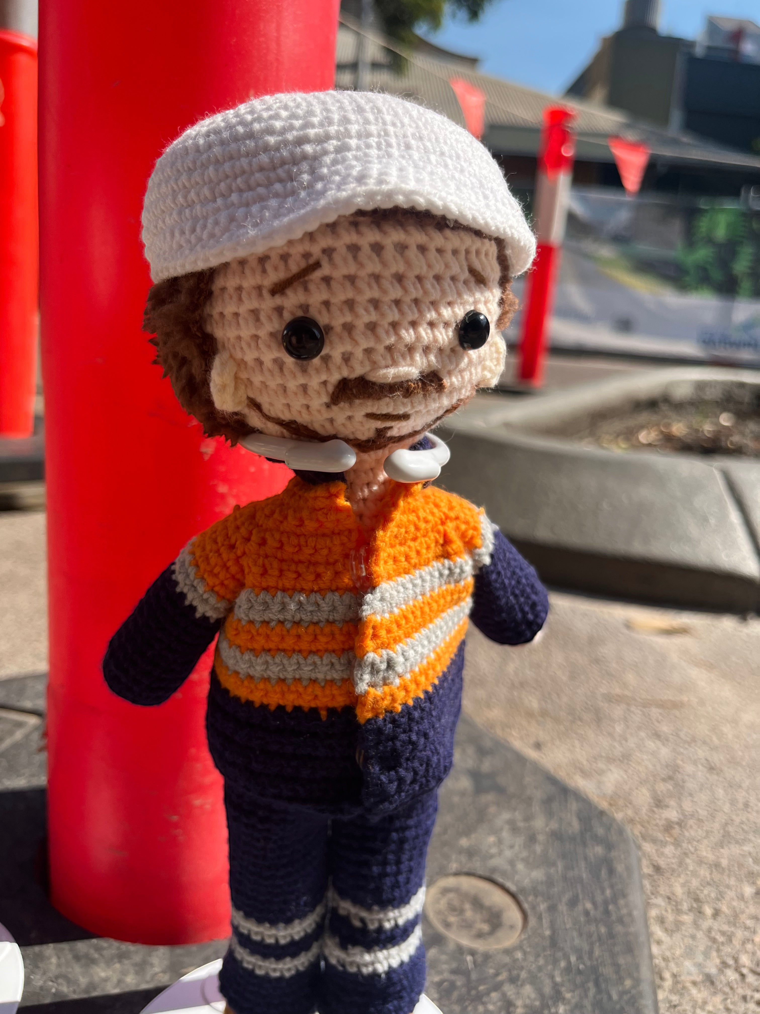Suzie's Sunshine Dolls orange hi-vis miner/tradie doll, crocheted with navy and grey stripes. White cap.