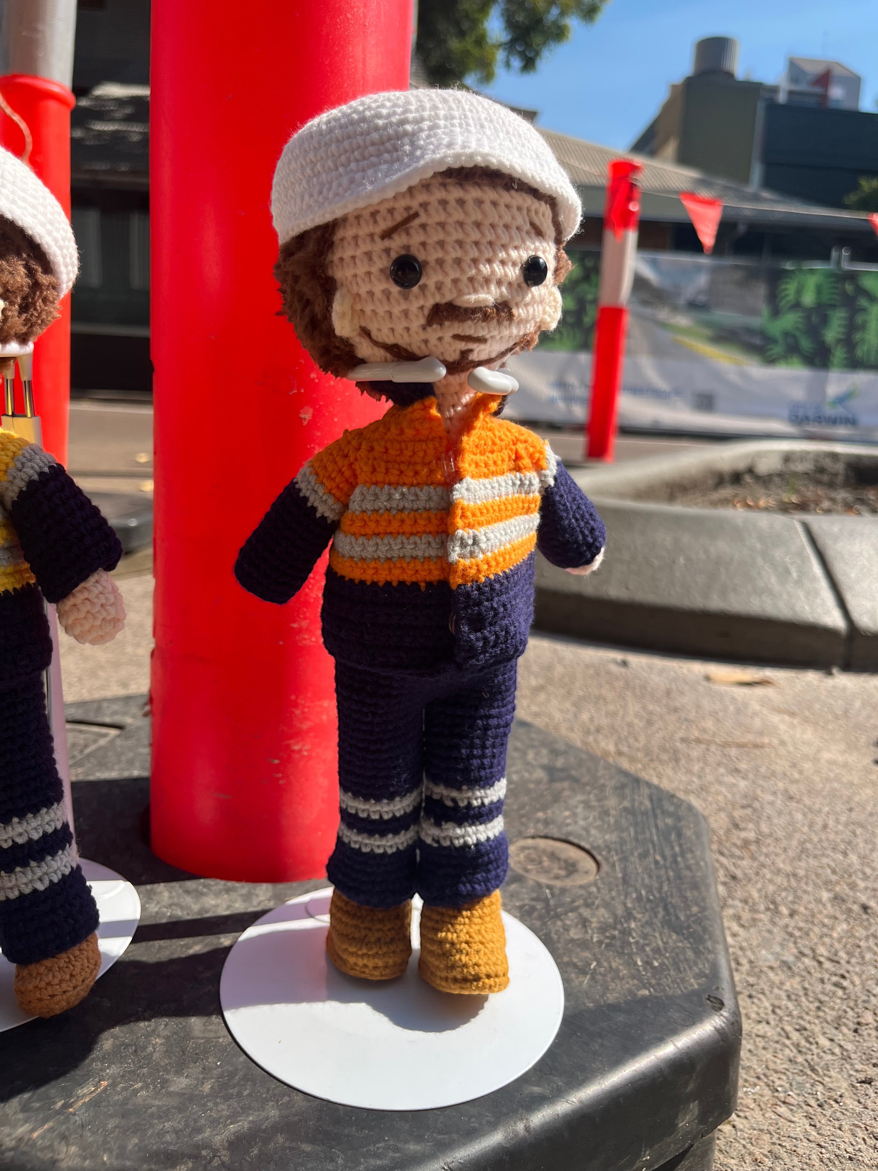 Suzie's Sunshine Dolls Orange Hi-Vis Miner/Tradie doll, crocheted with navy, orange, and grey stripes, white hat, and yellow boots.