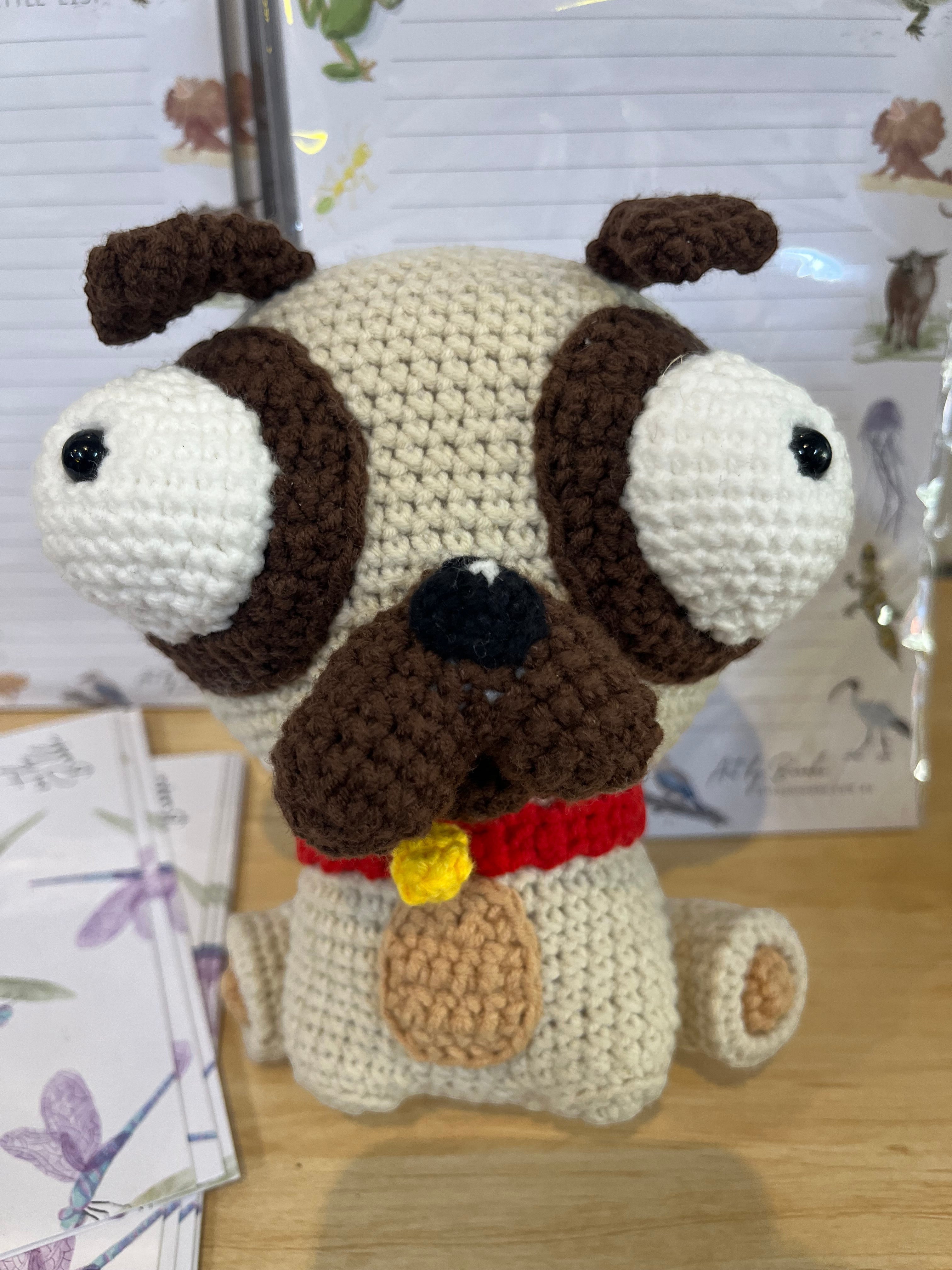 Suzie's Sunshine Dolls Pig the Pug crochet toy with big eyes, red collar, and yellow tag. Beige and brown yarn.