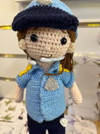 Suzie's Sunshine Dolls crocheted police officer doll in blue uniform with cap, badge, and yellow shoulder details.